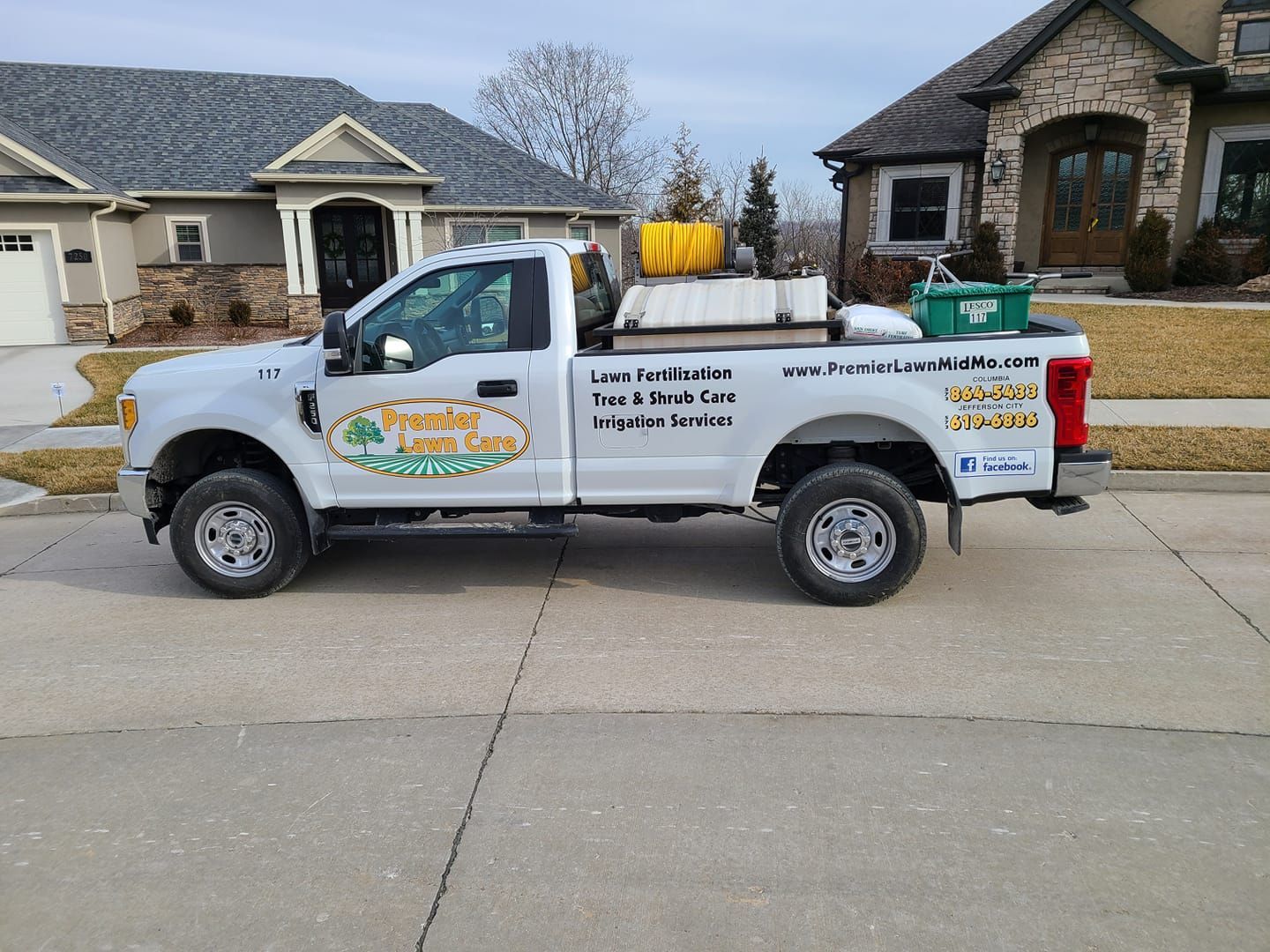 White utility truck with company signage parked on a suburban street in front of houses.