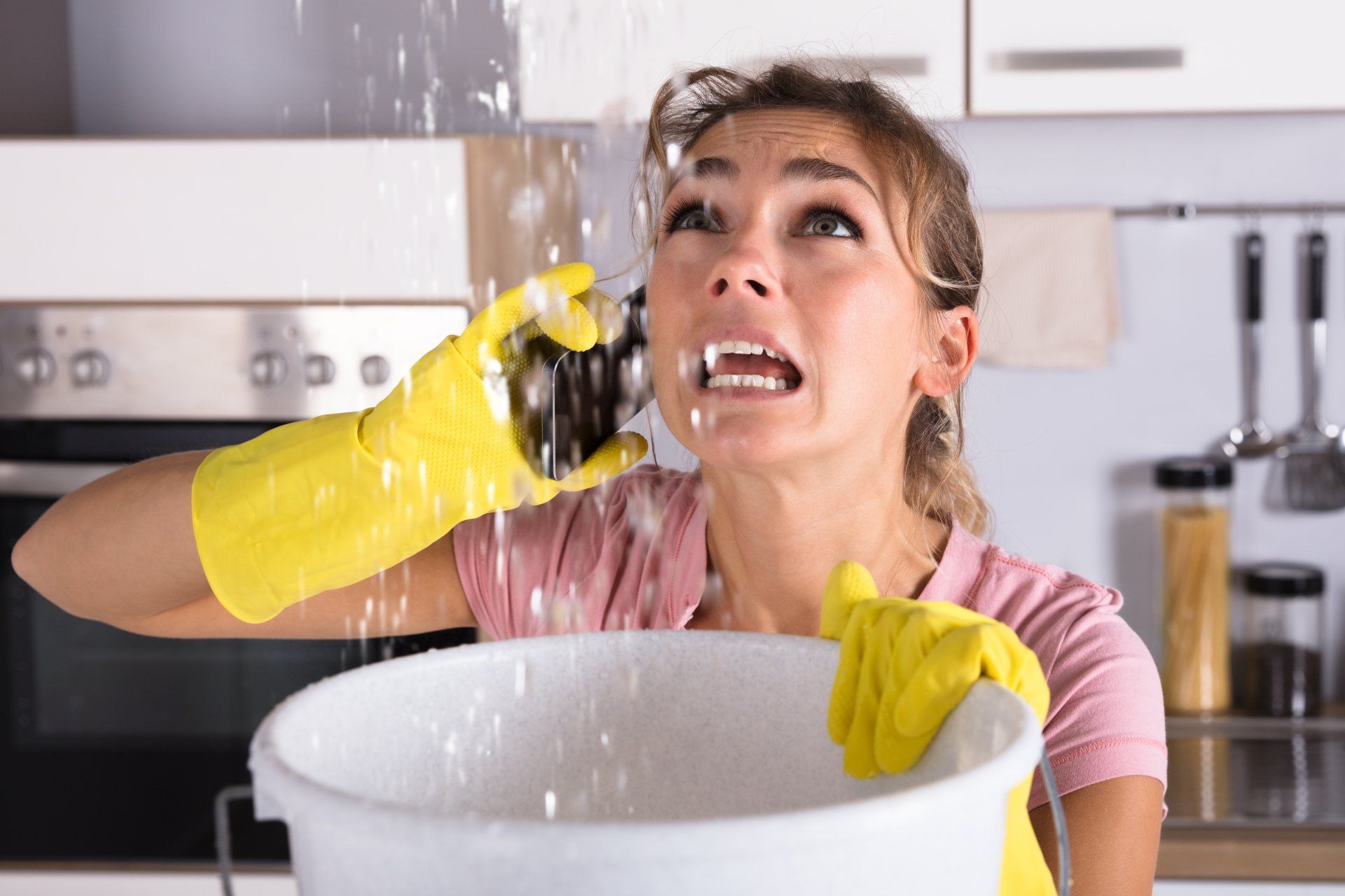 A woman is holding a bucket with water coming out of the ceiling.