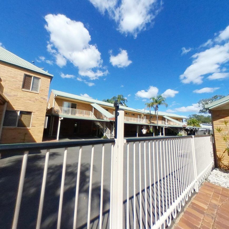 A White Fence With a Brick Building in the Background — Country Comfort Gin Gin Wild Scotsman Motor Inn in Gin Gin, QLD