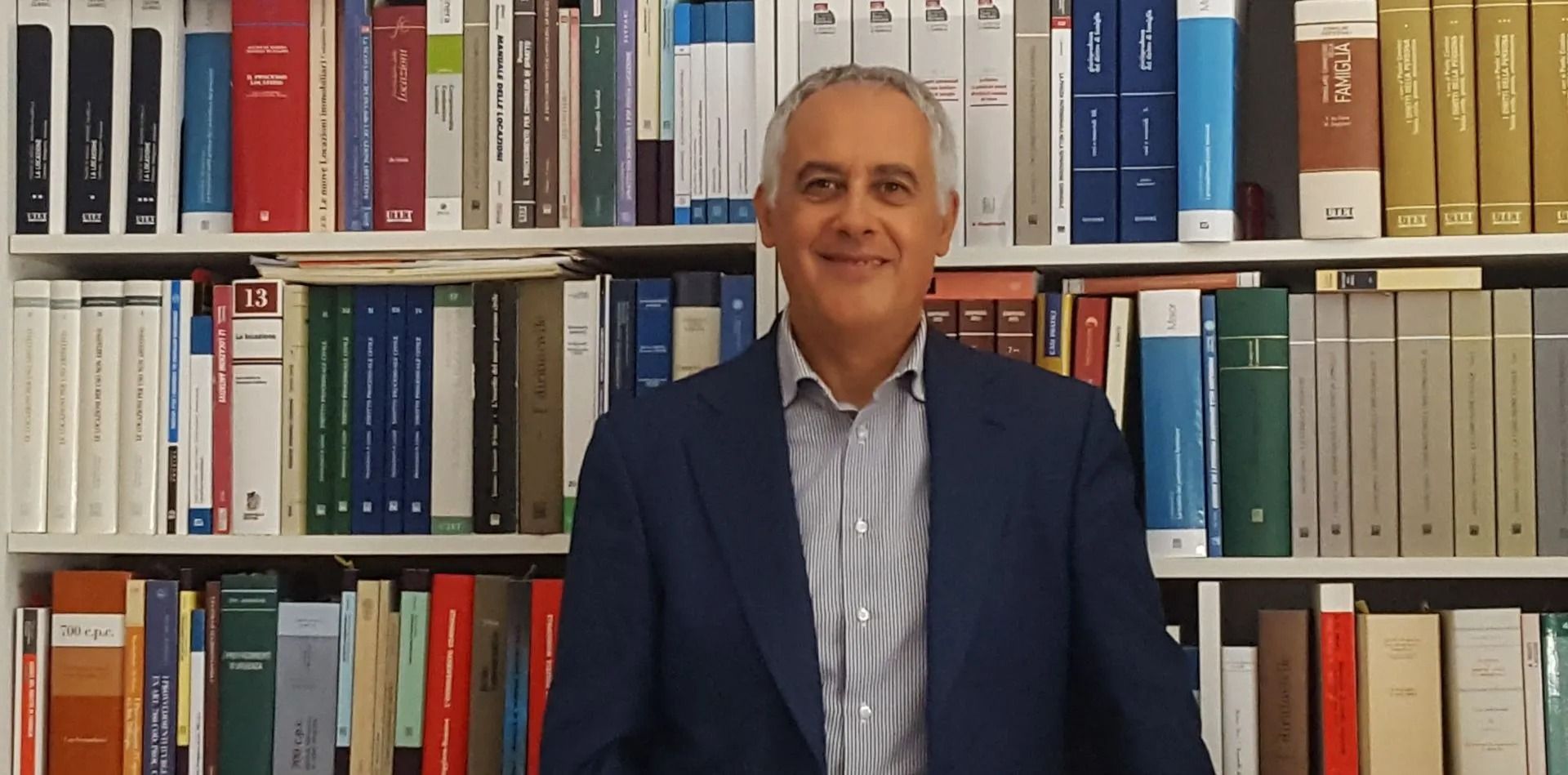 Un uomo con una giacca scura in piedi davanti a scaffali pieni di libri e raccoglitori