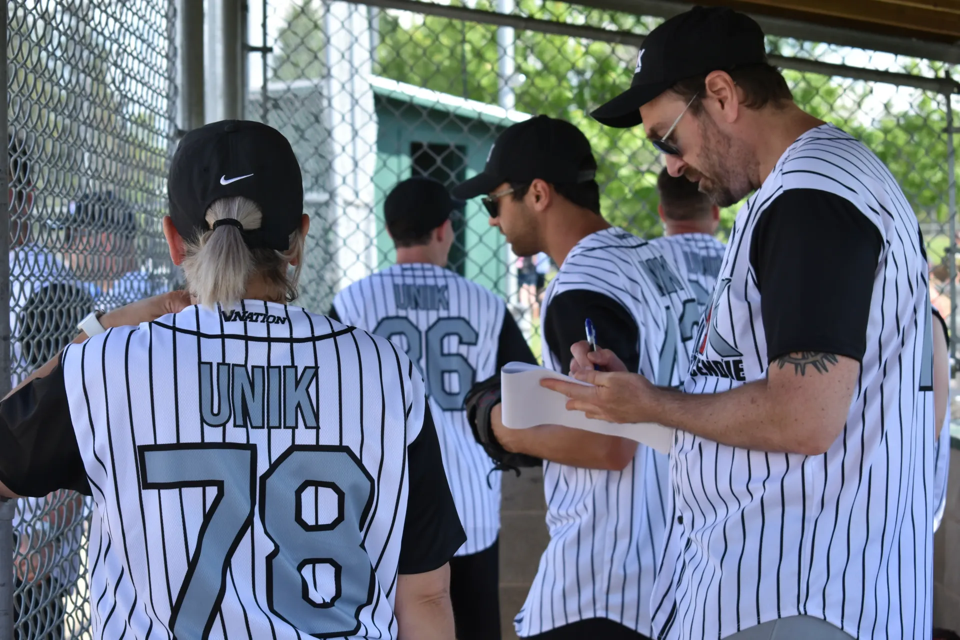 Les joueurs de UNIK en maillots à fines rayures noires et blanches se tiennent près d'une clôture, l'une d'elles écrivant sur un bloc-notes.