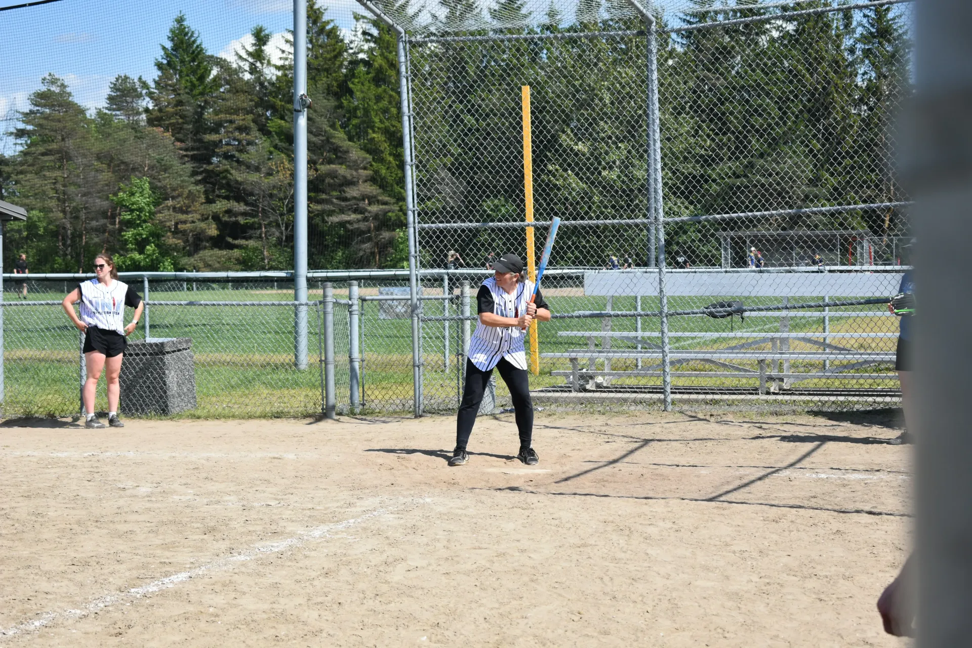 Joueuse de softball au marbre, avec l'arbitre et le receveur près d'un filet de protection en grillage sur un terrain ensoleillé