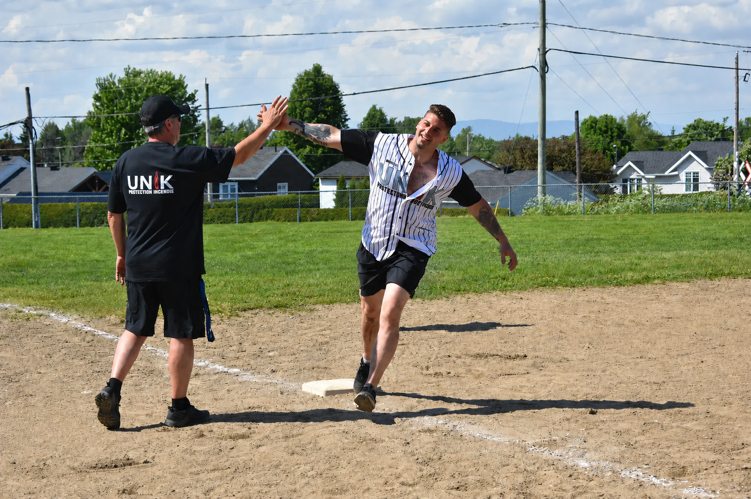 Deux joueurs se tapent dans la main au marbre sur un terrain de baseball sous un ciel ensoleillé.