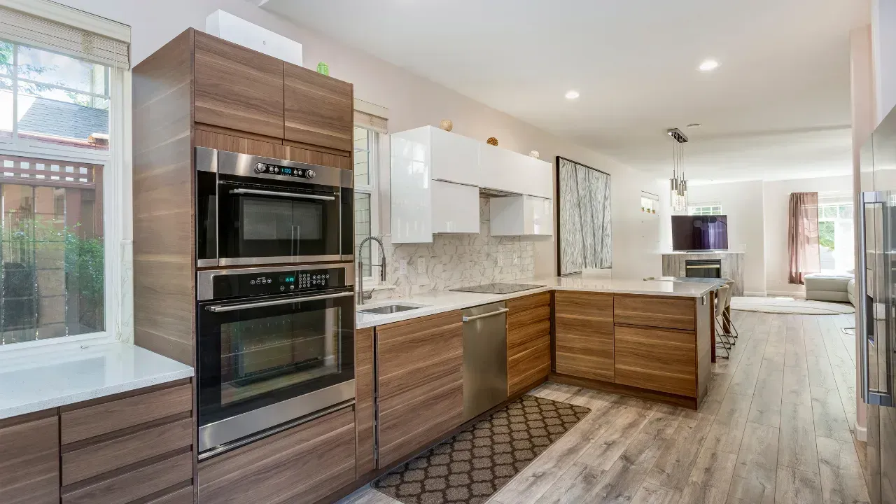 A wood styled kitchen with black and silver appliances, two ovens stacked on top of each other.