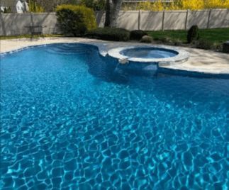 Blue swimming pool with an attached hot tub in a backyard setting.