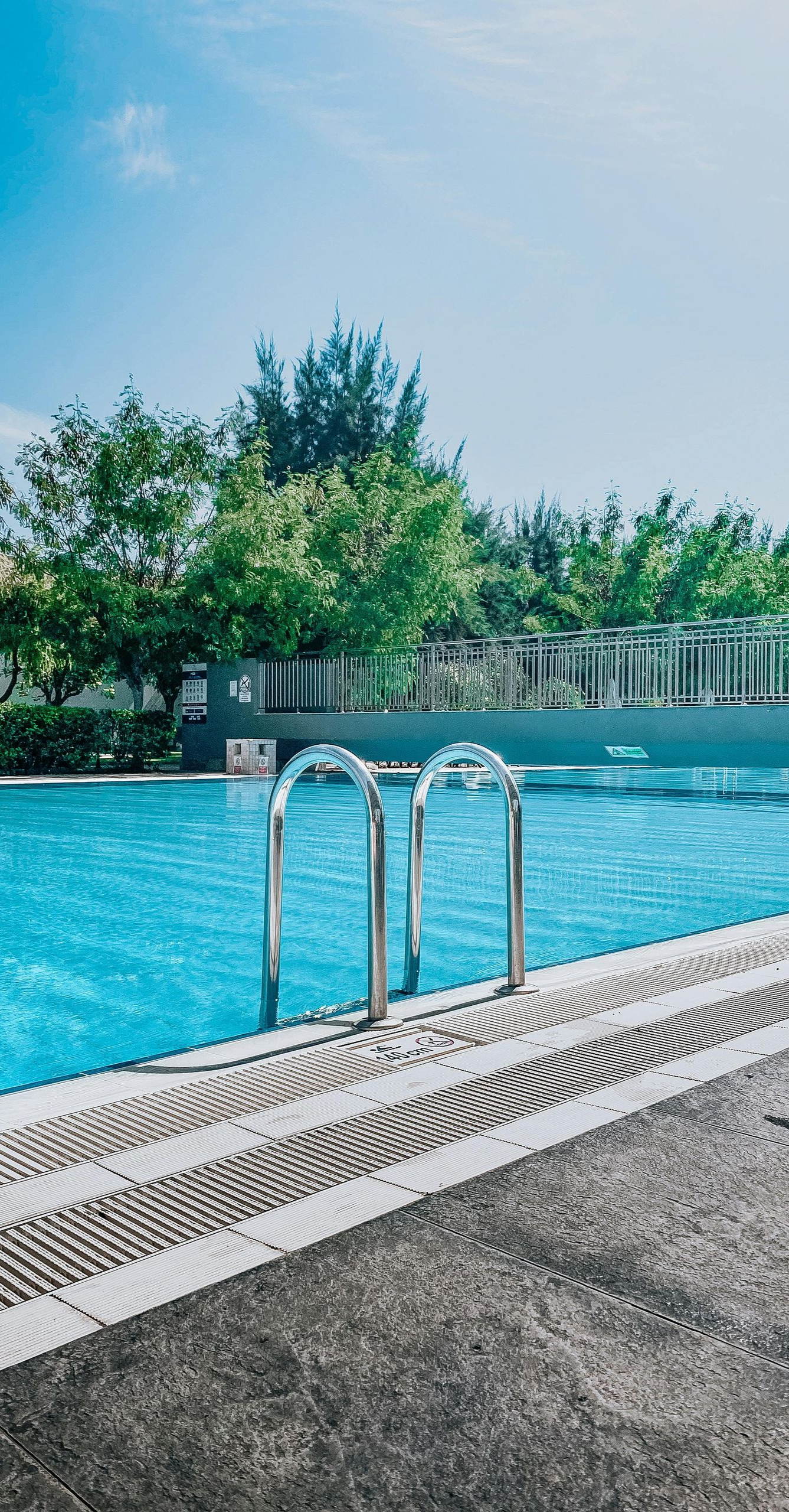 Swimming pool surrounded by green lawn and landscaping. Black fence borders the pool.