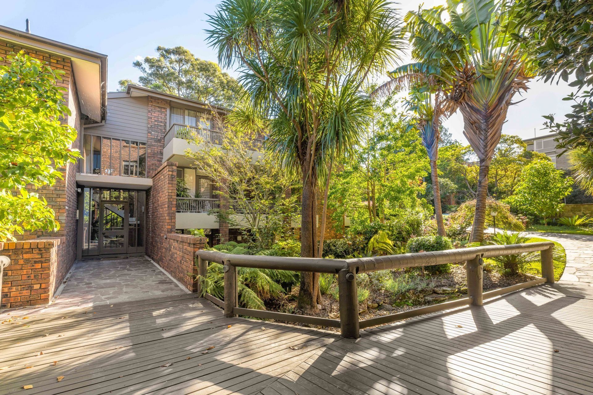 A brick building with a wooden walkway leading to it surrounded by trees and bushes.