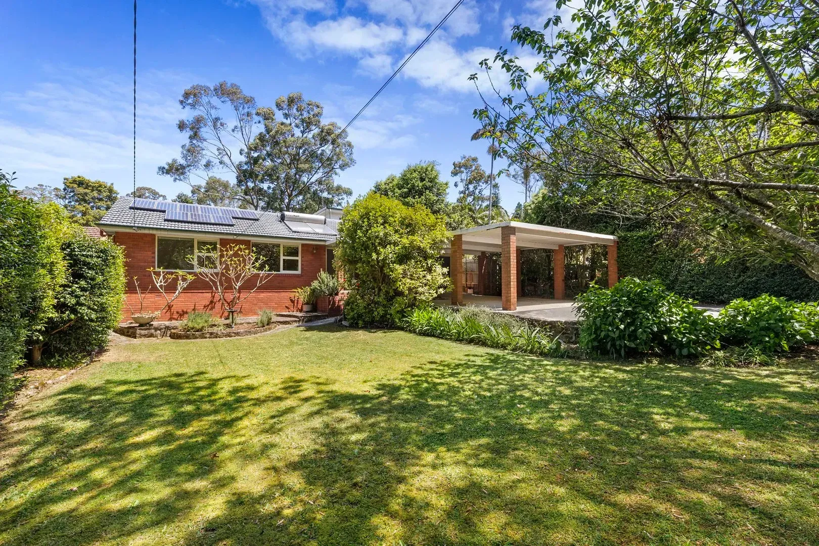 Single-story brick house with a covered patio, surrounded by a green lawn and trees under a blue sky