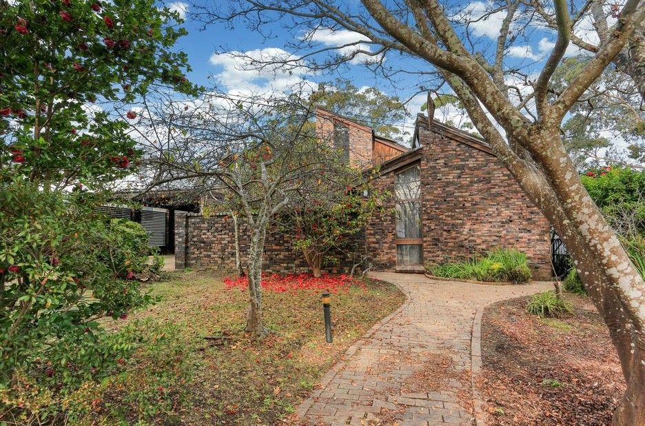 Brick house with a curved walkway, trees, and red flowers in a landscaped yard