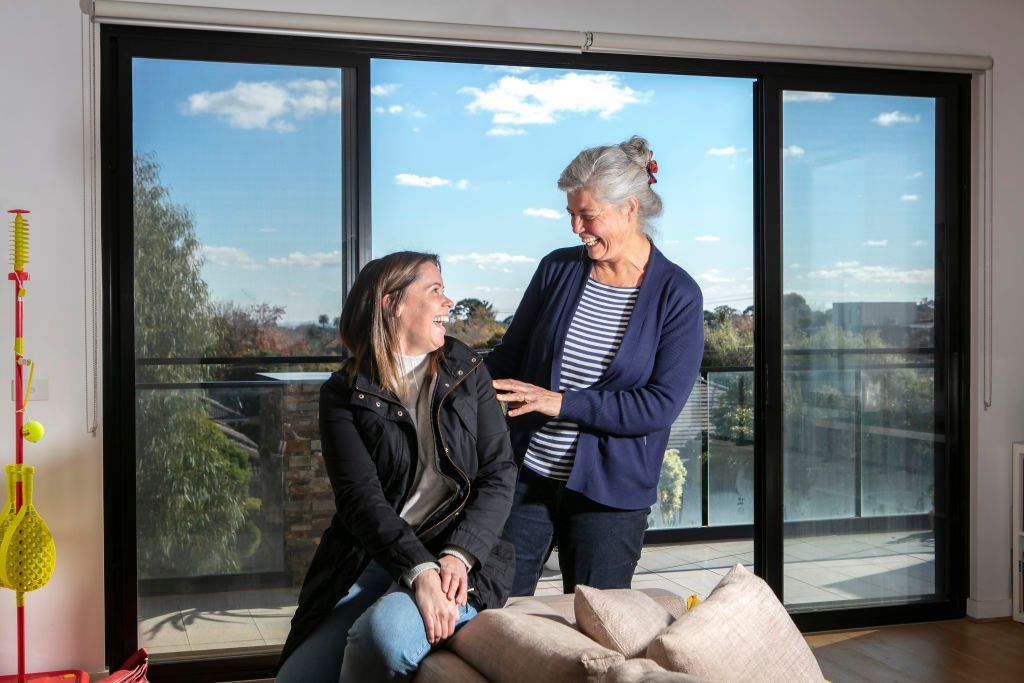 Two women are sitting on a couch in front of a large window.