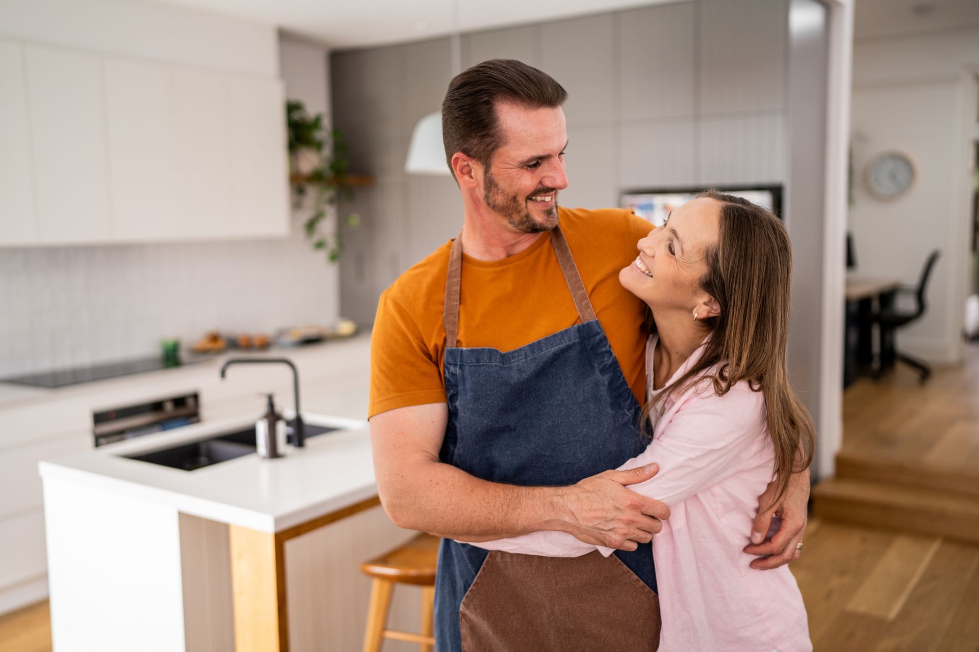 A man in an apron is hugging a woman in a kitchen.