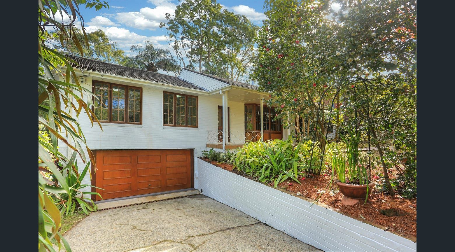 Modern white house with a wooden garage door, driveway, and landscaped front yard surrounded by trees