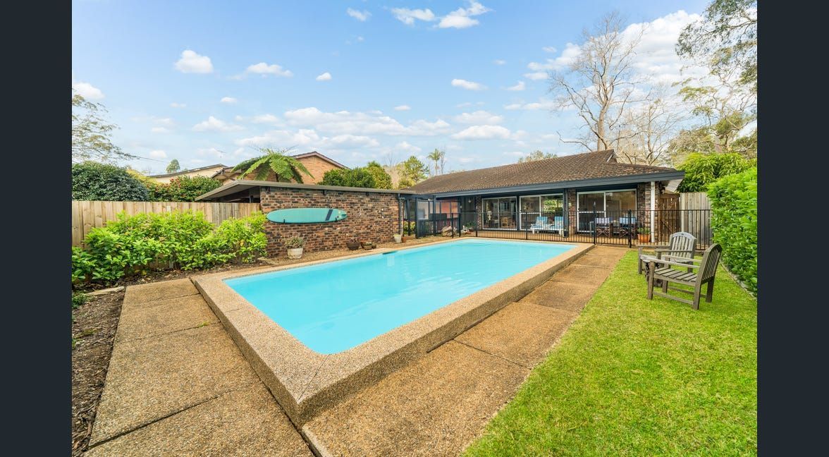 Backyard swimming pool beside a patio and lawn under a partly cloudy sky