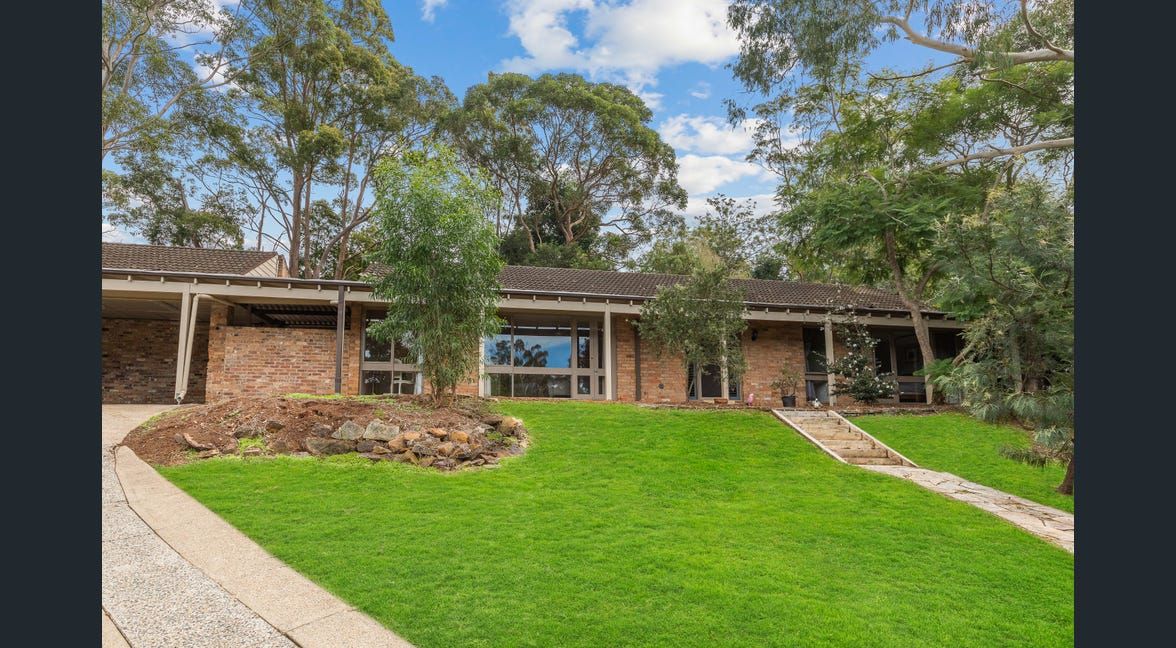 Brick house with a green lawn and trees in a wooded yard