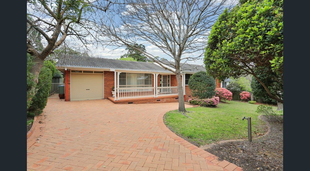 Brick driveway leading to a single-story house with a garage and front garden, framed by leafless trees.