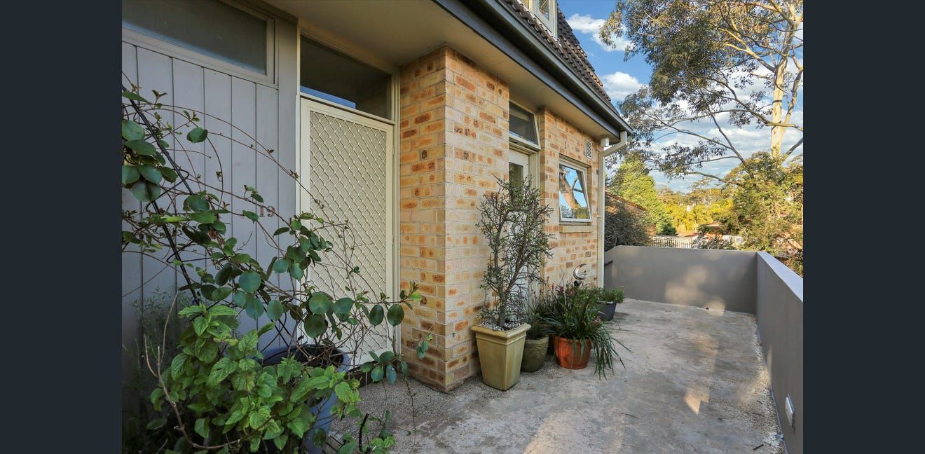 Stone house entryway with potted plants and a gravel path beside a garden wall