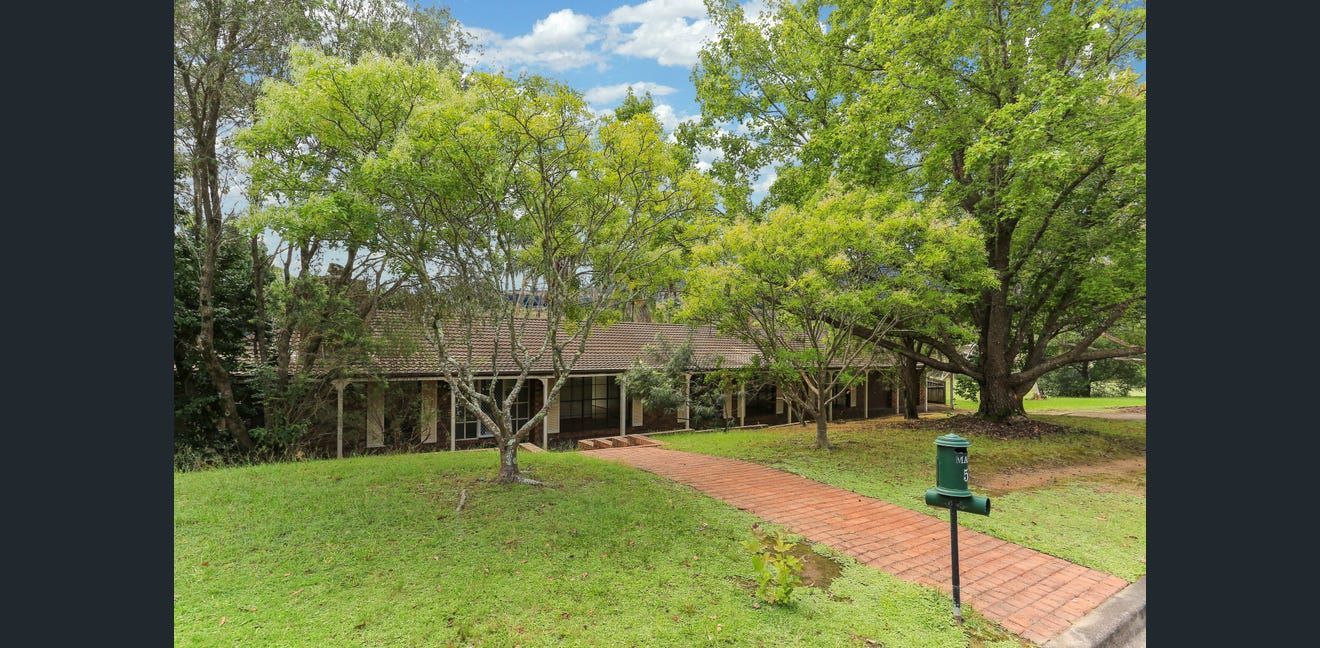 Brick path through a green park with trees and a wooden bridge under a cloudy sky