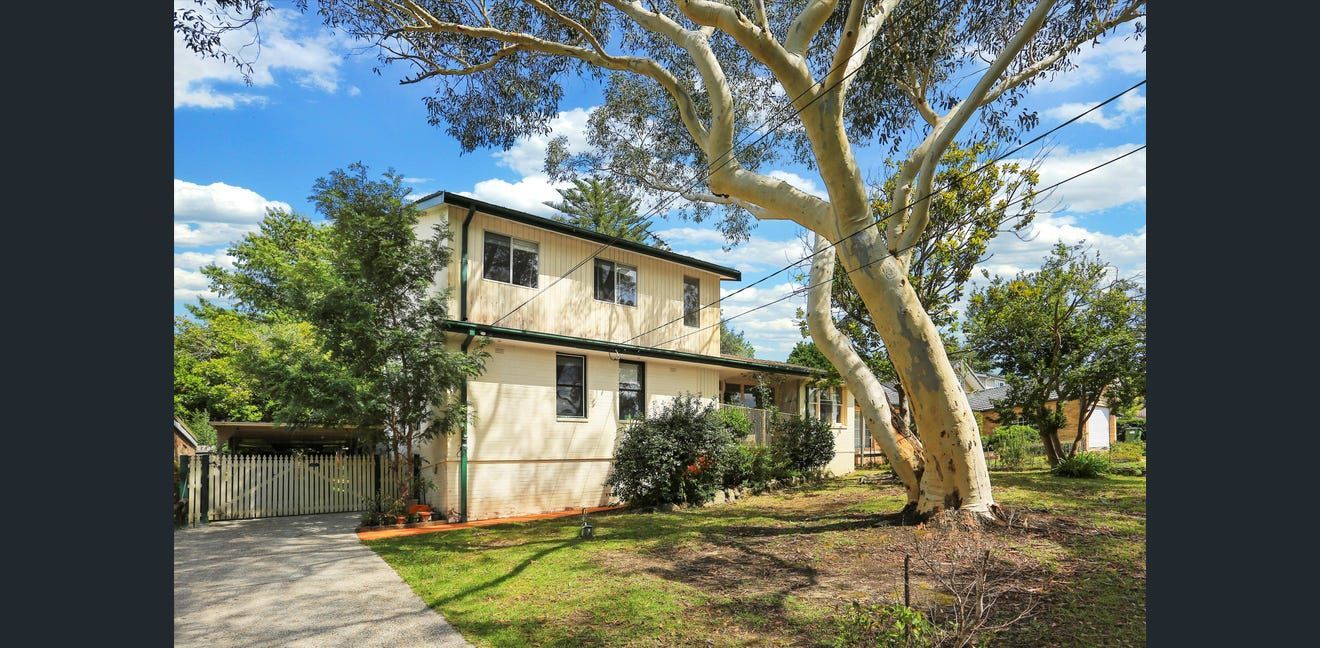 Two-story tan house with a large tree and green yard on a sunny day