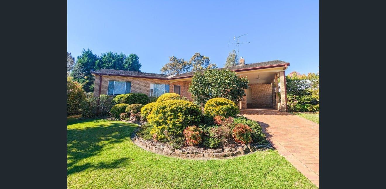 Single-story house with a manicured front yard, flower bed, and driveway in bright sunlight