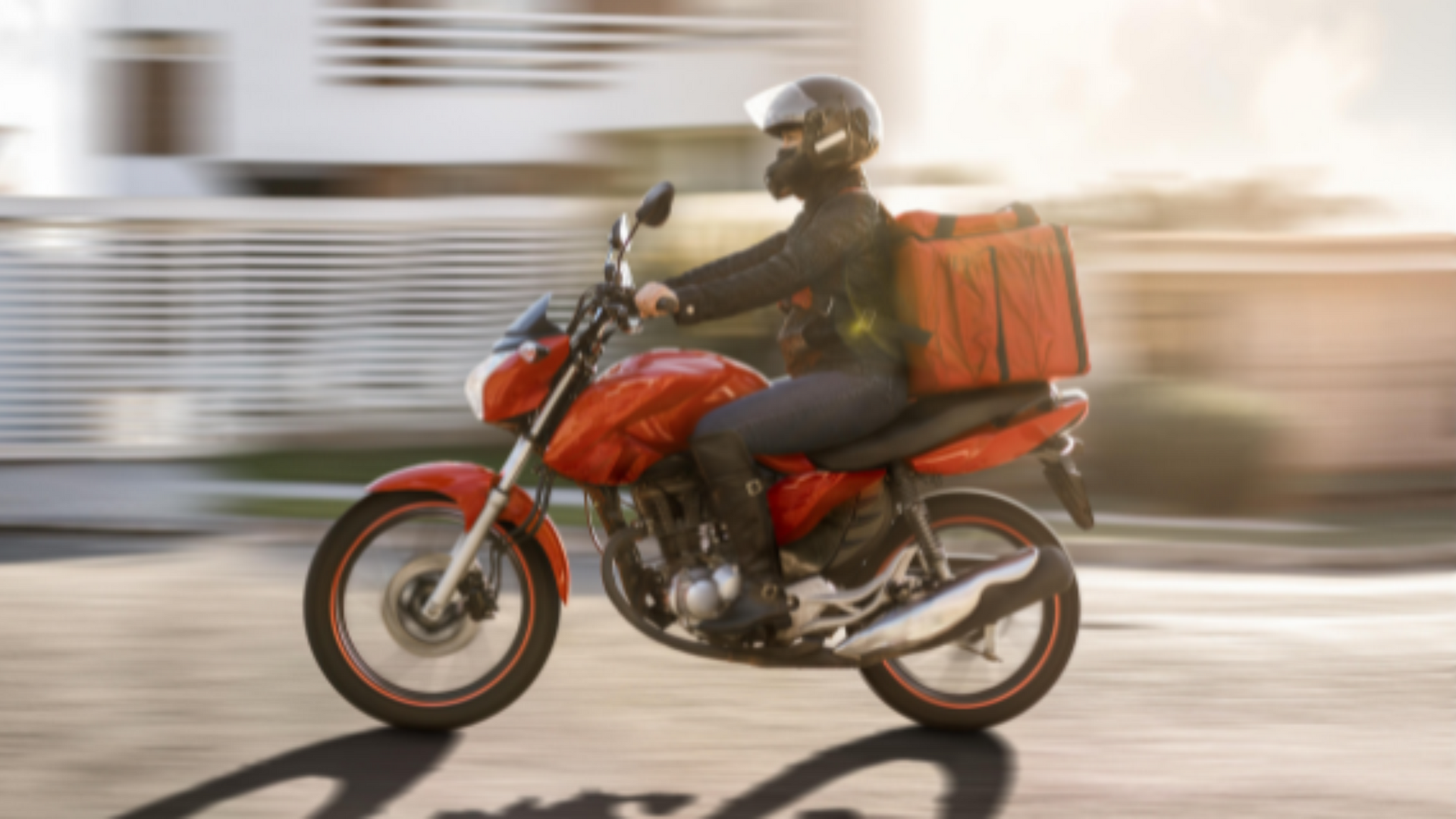 Um entregador está andando em uma motocicleta vermelha por uma rua.