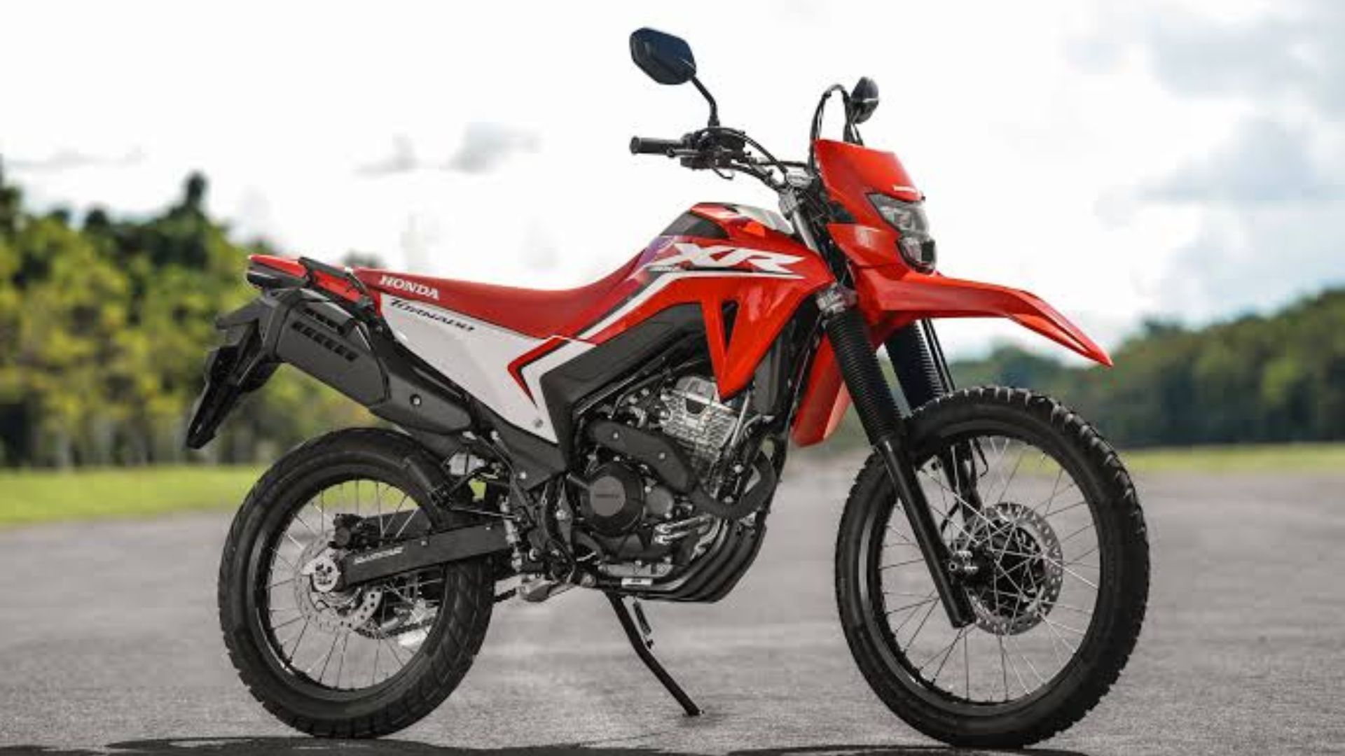Red and white off-road motorcycle parked on a paved road with a grassy field in the background