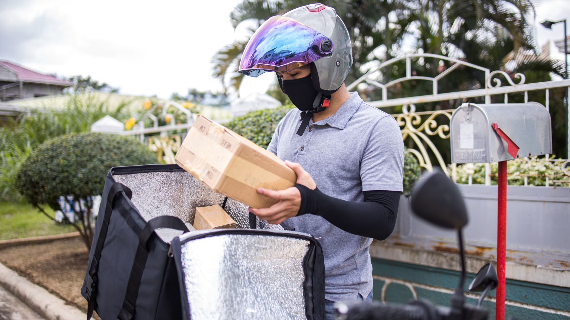 Person in a helmet reads a package beside a cargo bike in a residential driveway.