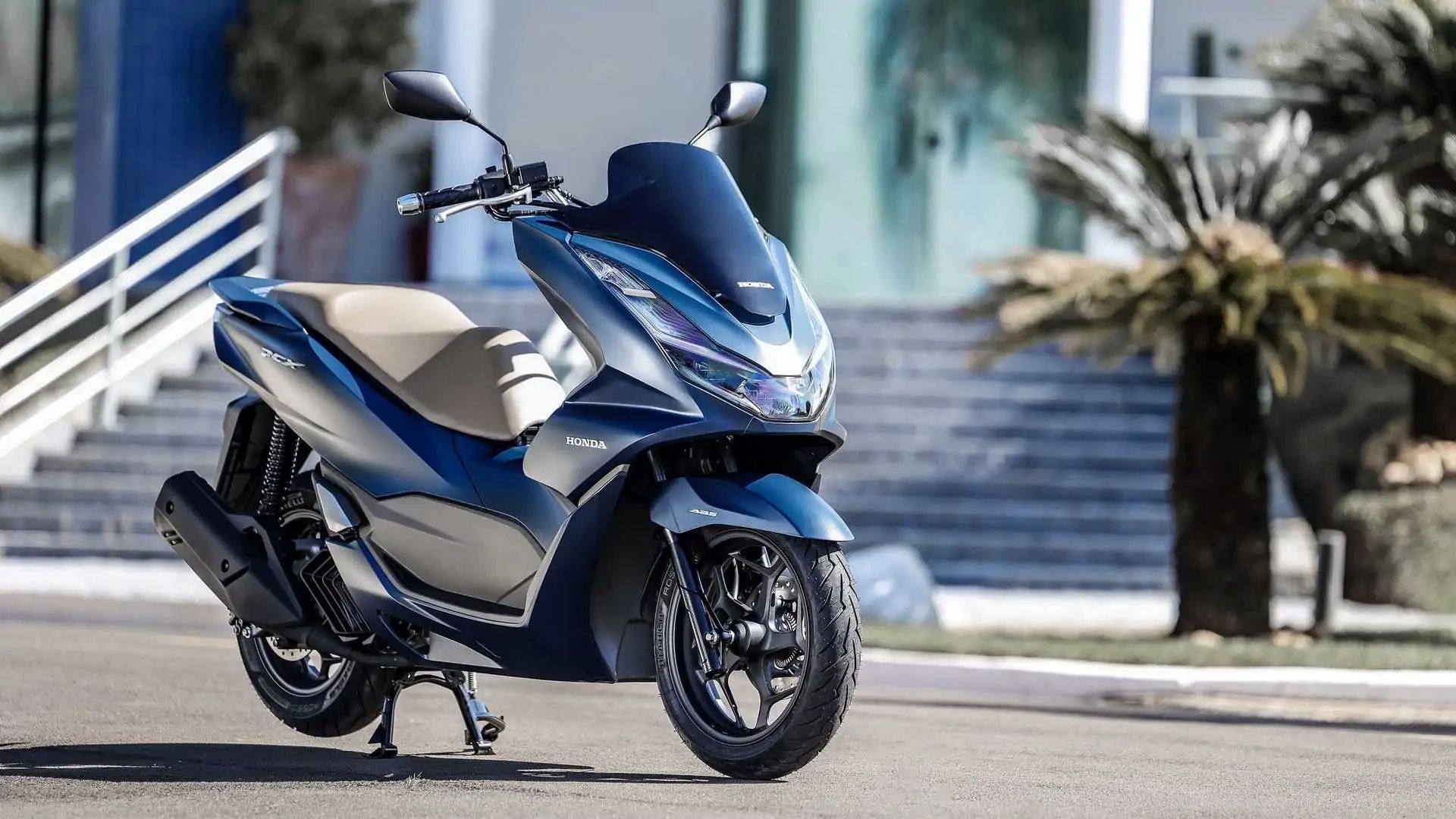Blue and beige scooter parked outdoors in front of stone steps and palm trees