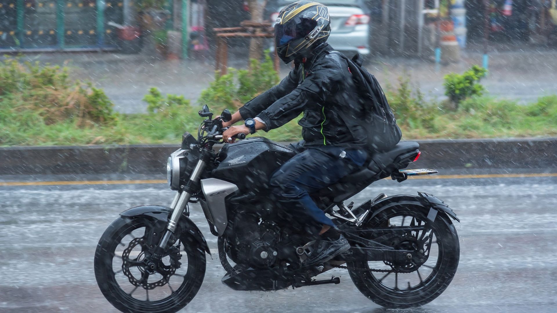 Motorcyclist in black gear riding through heavy rain on a wet city street