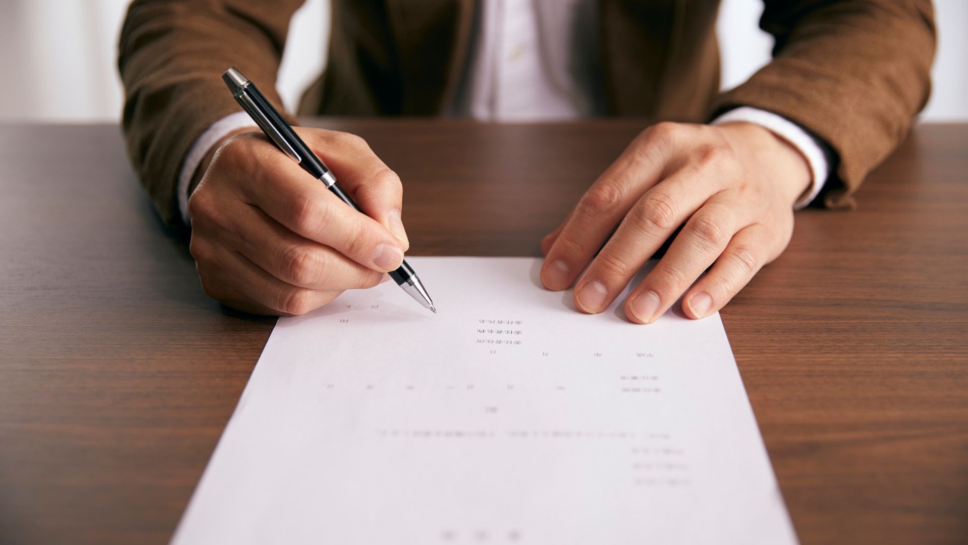 Hands signing a document on a wooden desk with a pen.