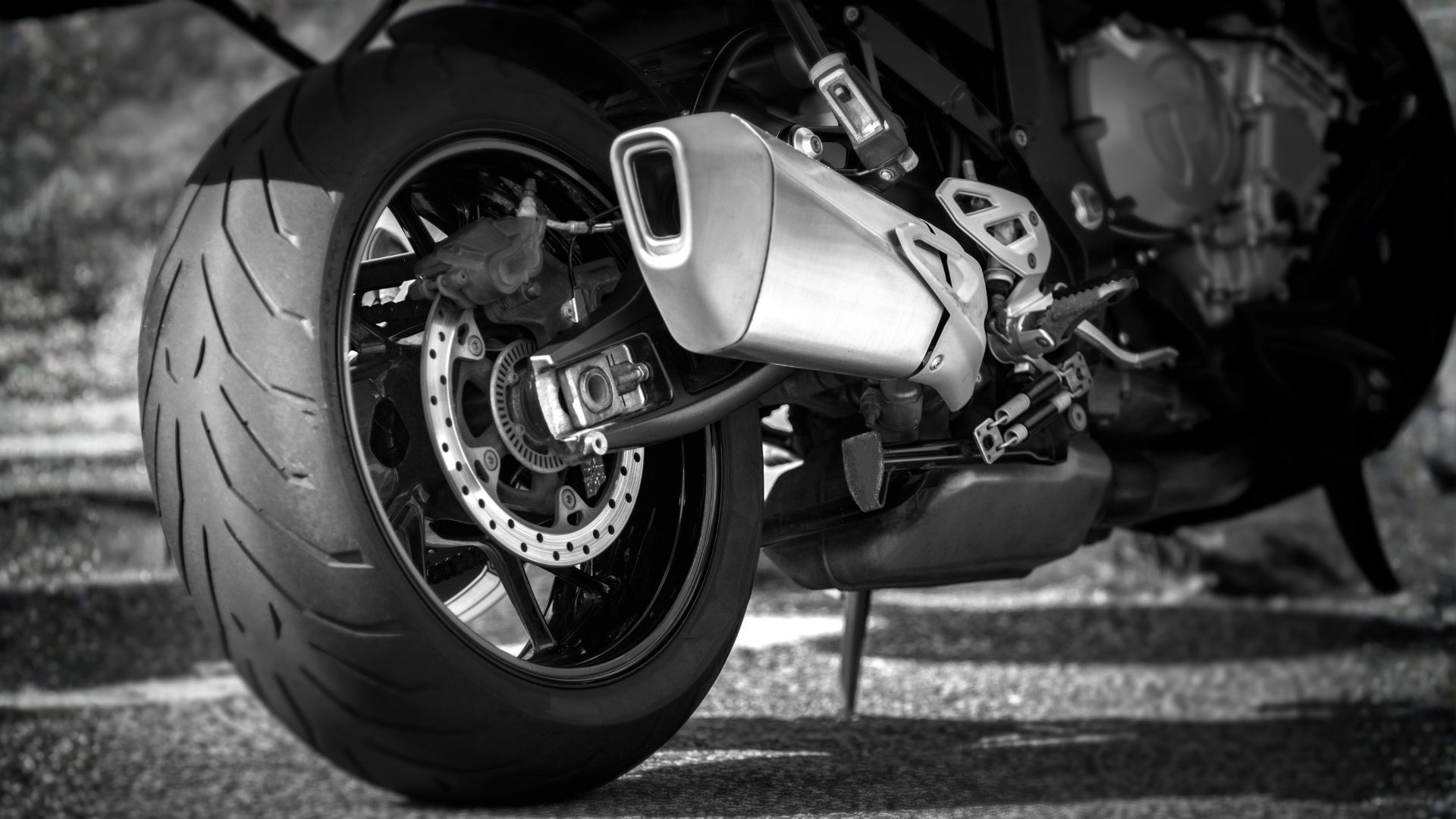 Close-up of a sport motorcycle’s rear wheel and exhaust, in black and white.