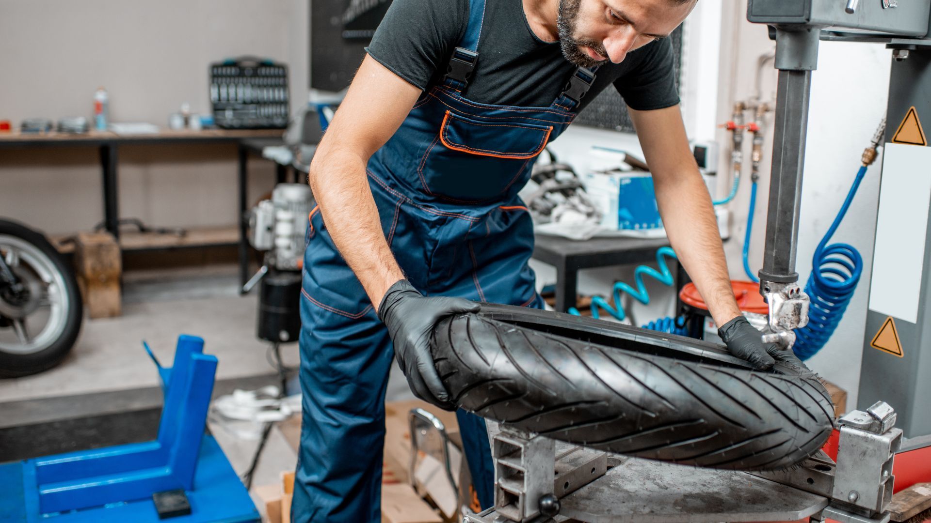 Mechanic in blue overalls inspects a car tire in an auto repair shop