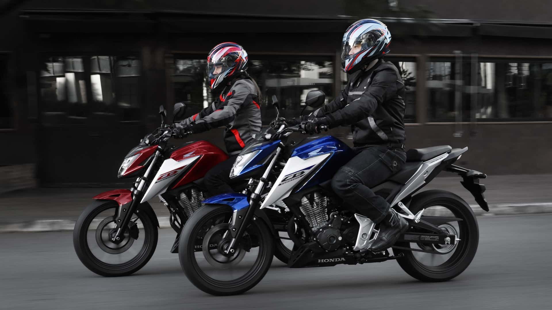 Two motorcyclists riding red and blue scooters side by side on a city street at night
