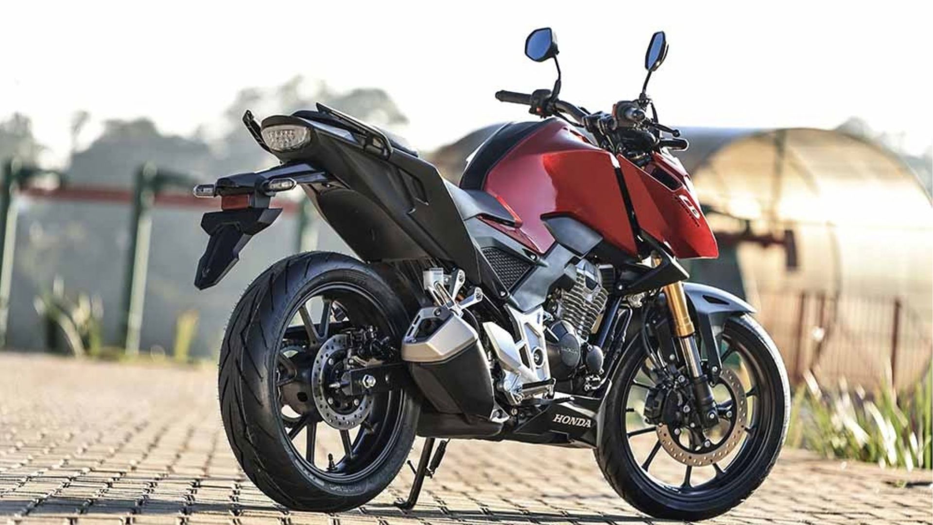Black and red sport motorcycle parked on a sunlit cobblestone path outdoors.