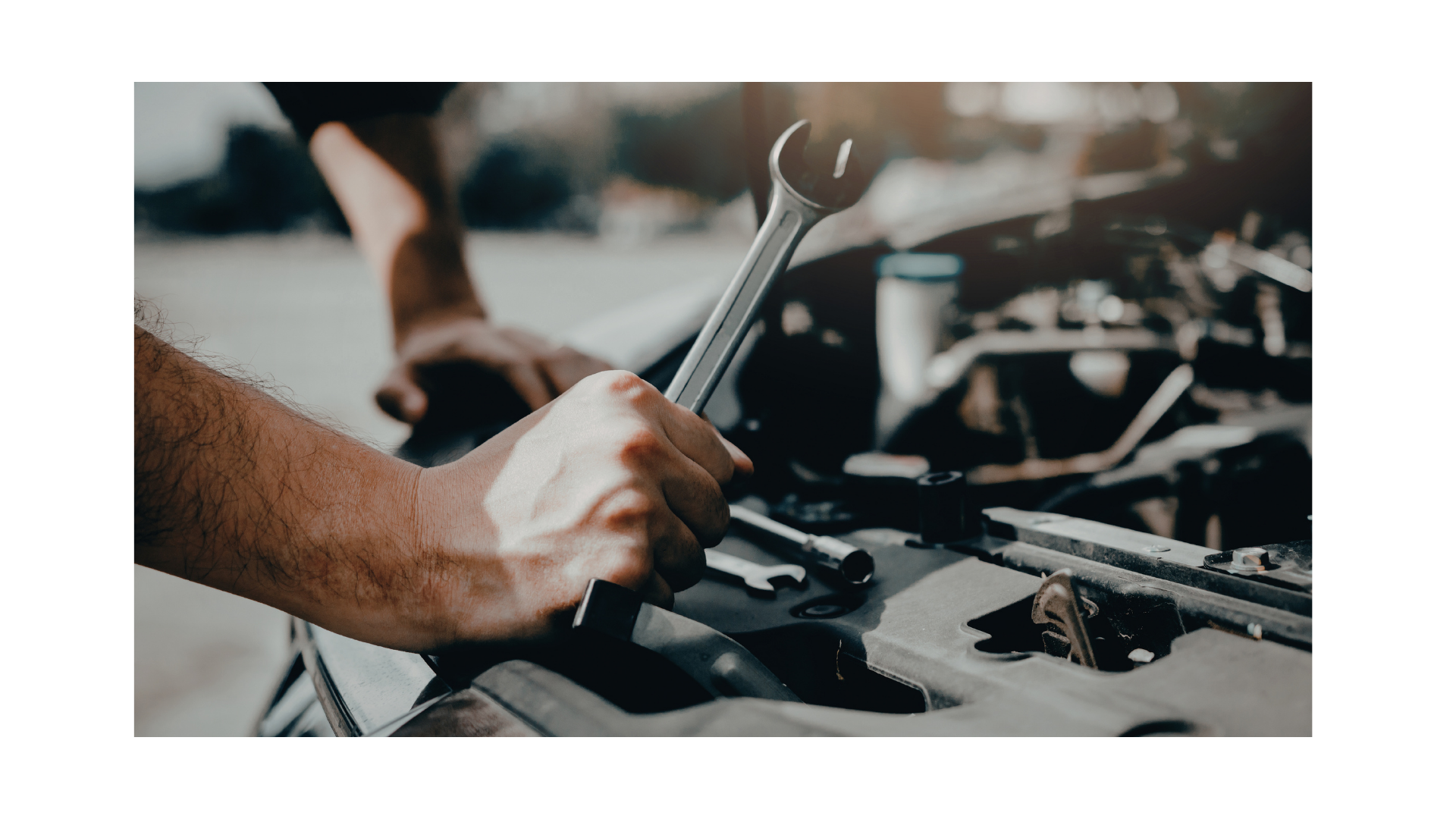 Mechanic’s hand holding a wrench over an open car engine in a garage