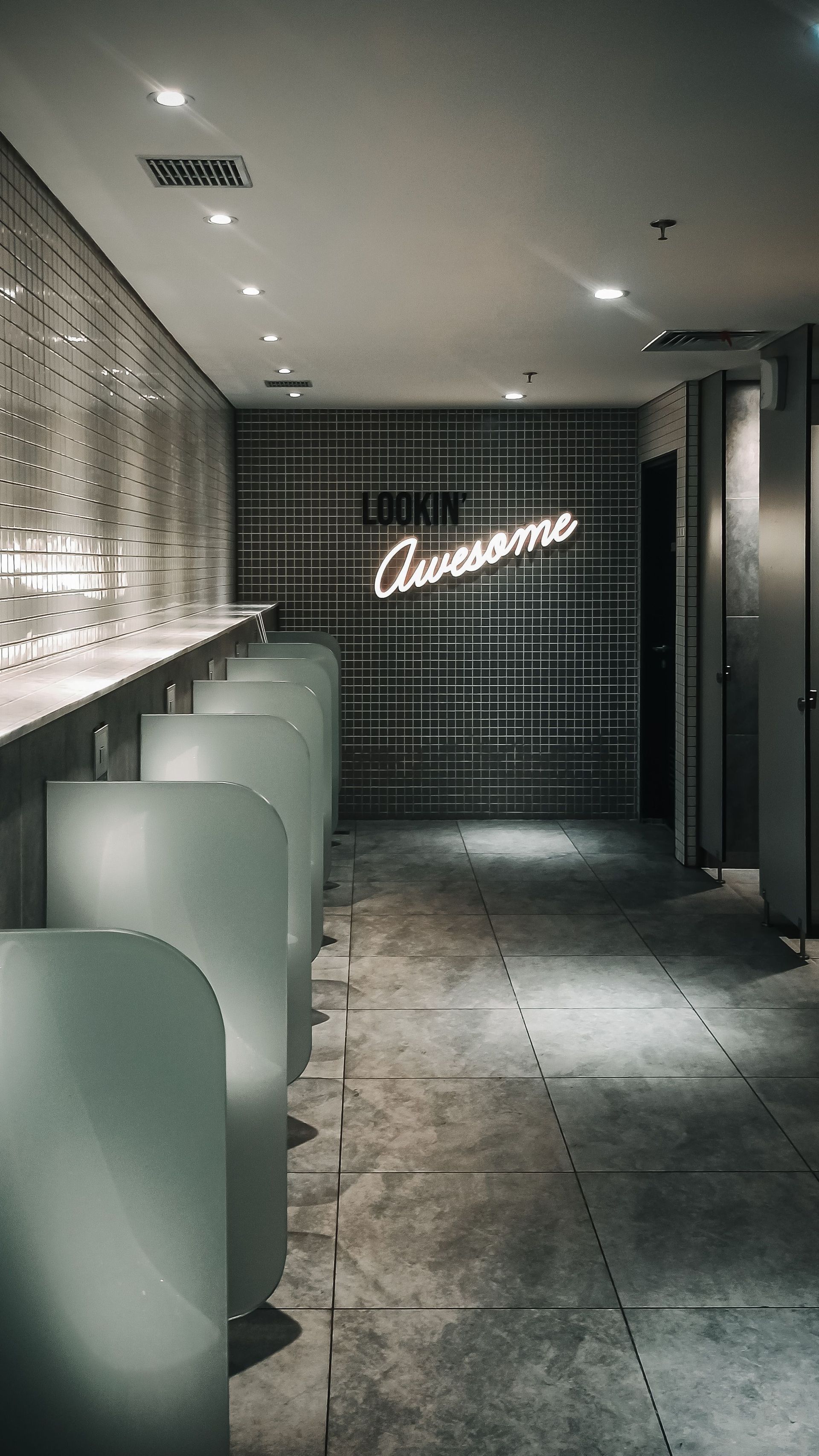 Dim corridor with white booths, dark tiled wall, and a glowing cursive neon sign ahead.