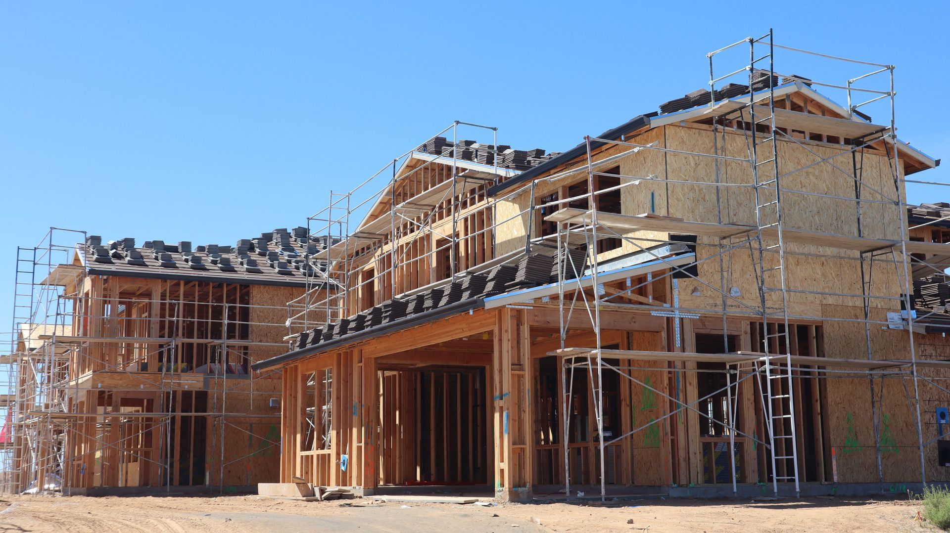 Wood-framed houses under construction with scaffolding and a clear blue sky