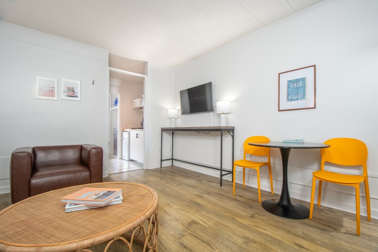 Bright living room with brown sofa, TV, wicker coffee table, and small yellow table with chairs