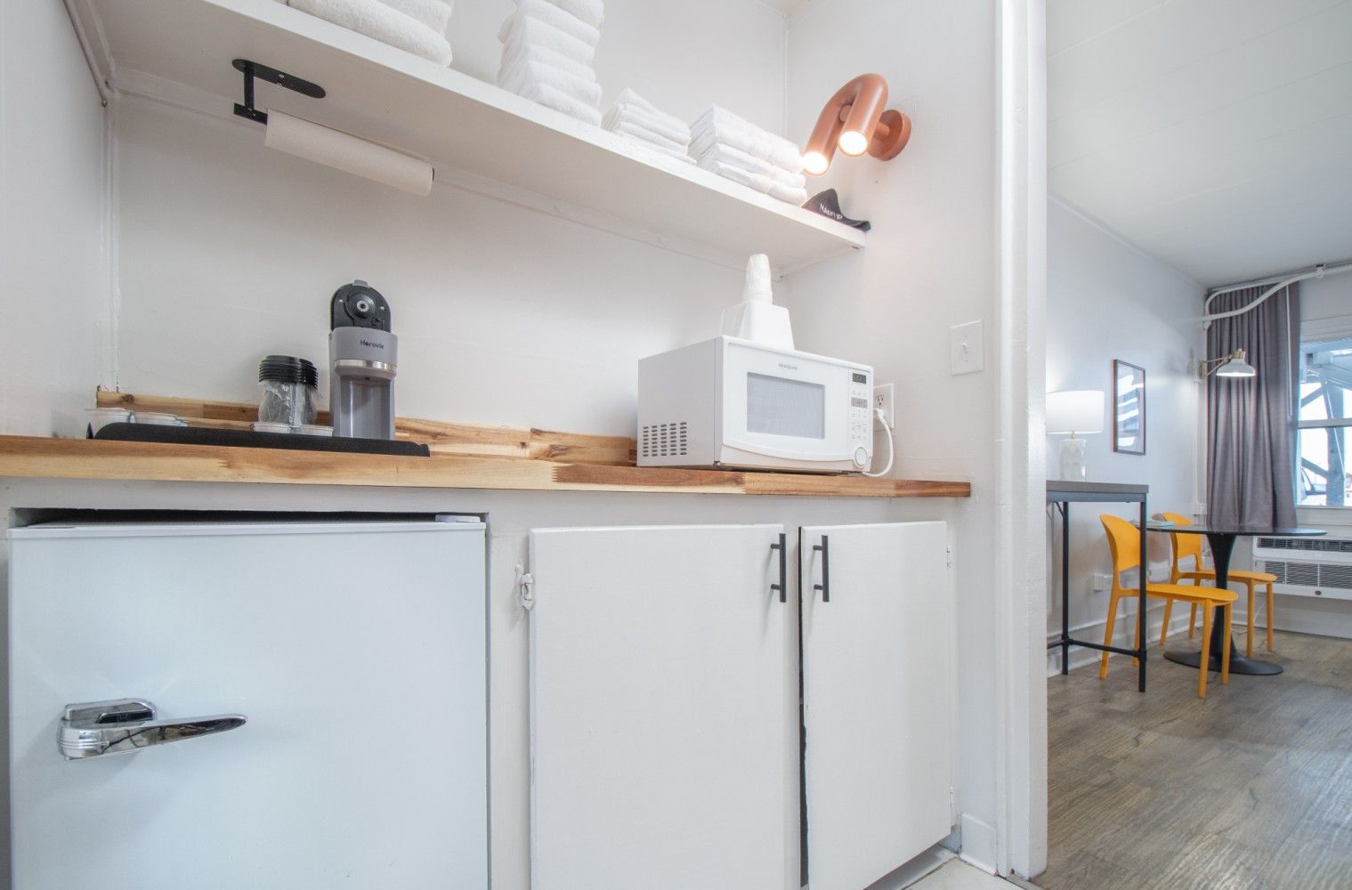 Small kitchen with white cabinets, wood countertop, retro fridge, and microwave beside a dining area