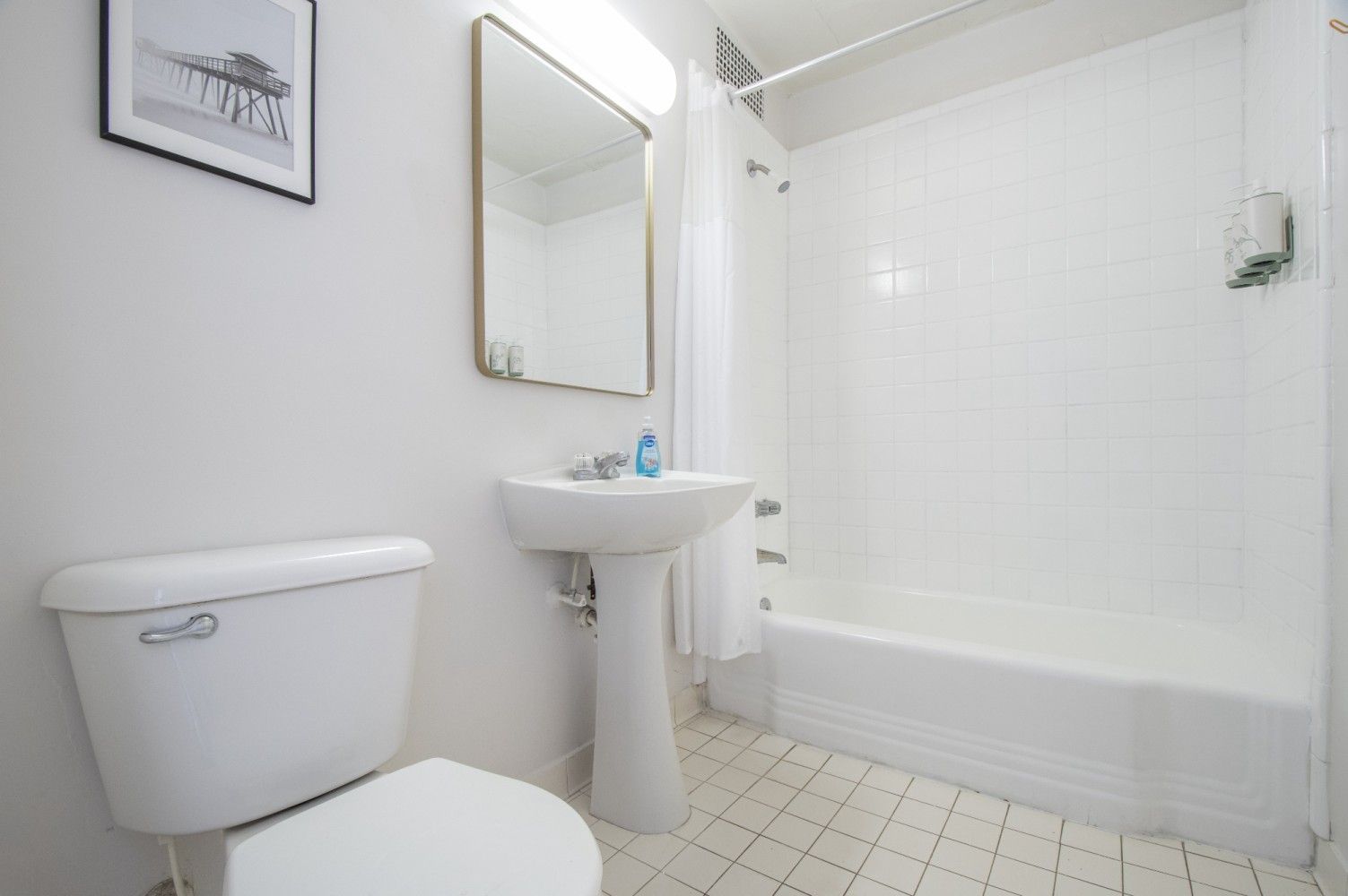 Small white bathroom with toilet, pedestal sink, mirror, and tub-shower combo