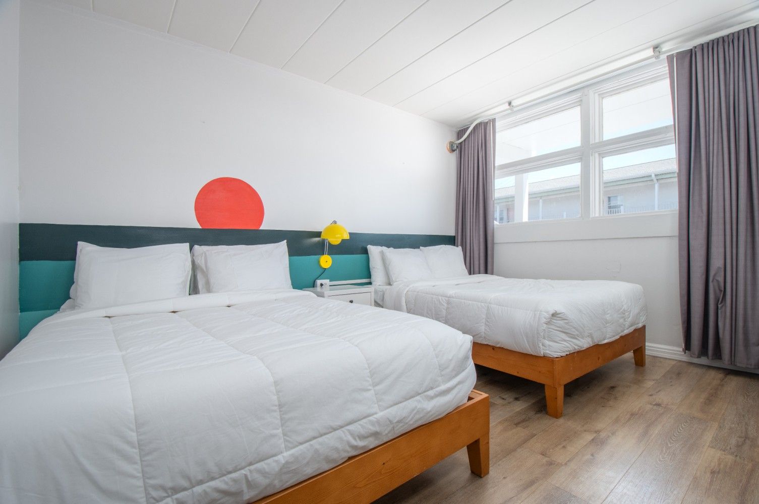 Bright bedroom with two white beds, teal headboards, gray curtains, and a red wall circle