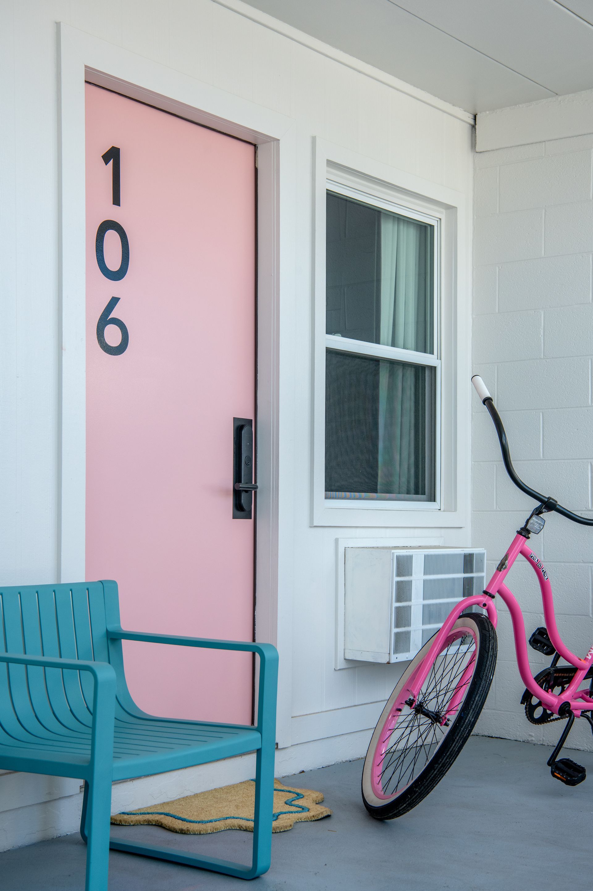 Pink front door with house number 106, turquoise chair, and pink bicycle on a porch