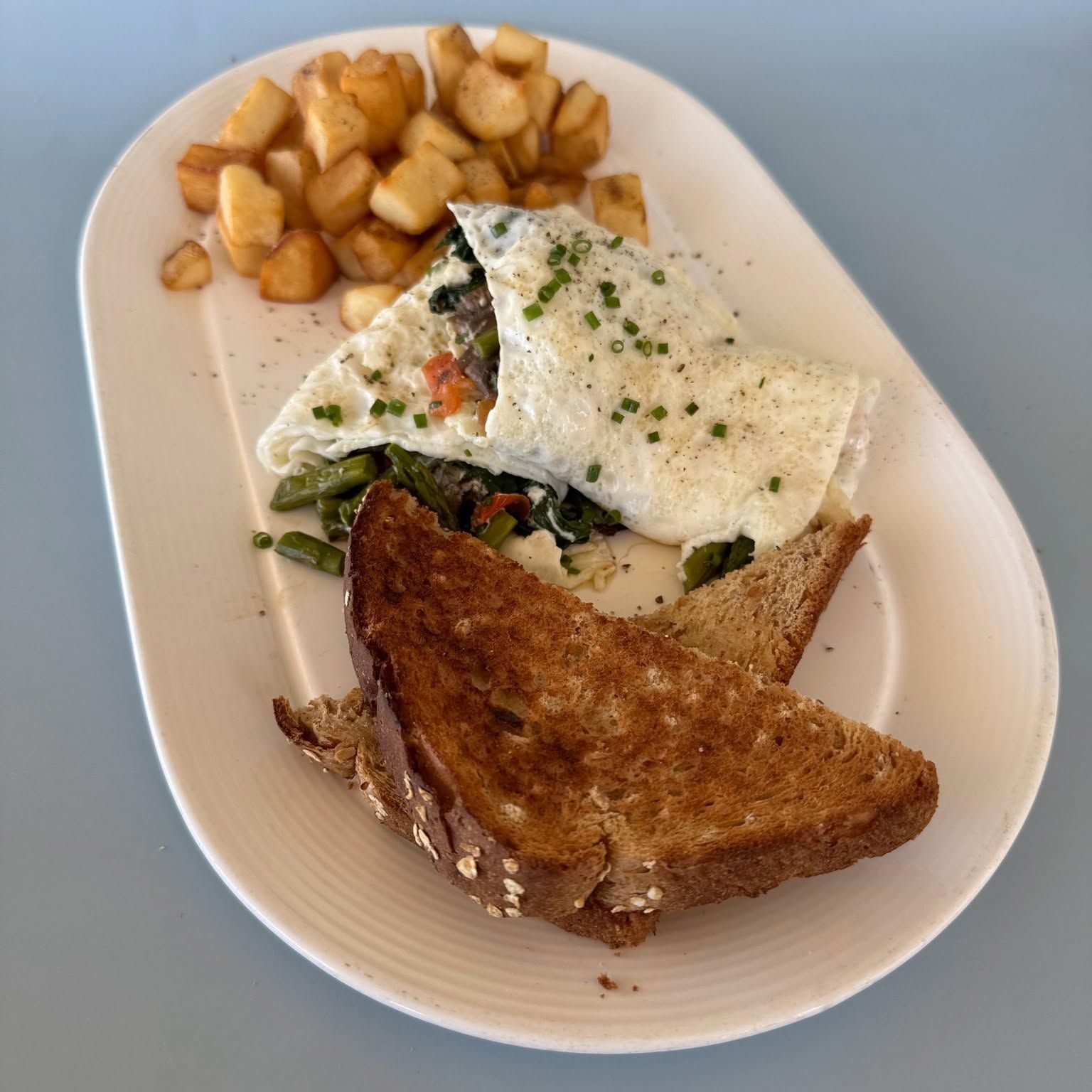 Plate with a sandwich, herb omelet, and diced potatoes on a white dish