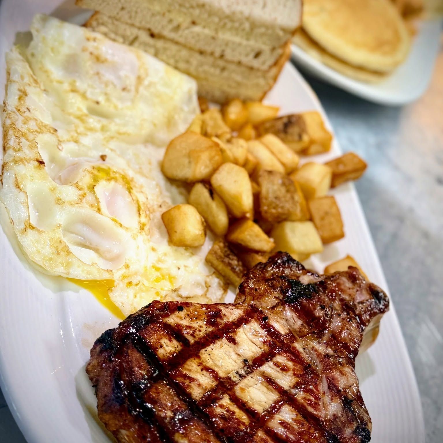 Steak with grill marks, eggs, home fries, and toast on a white plate