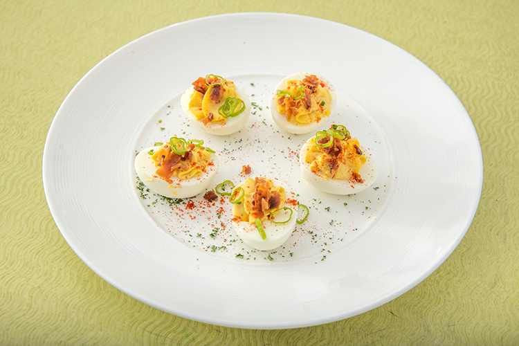 Deviled eggs topped with paprika and herbs on a white plate