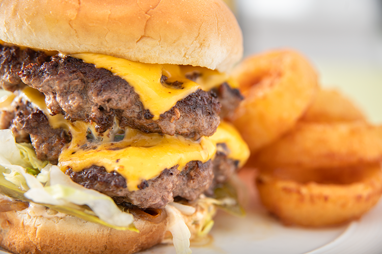 Double cheeseburger with onion rings on a white plate