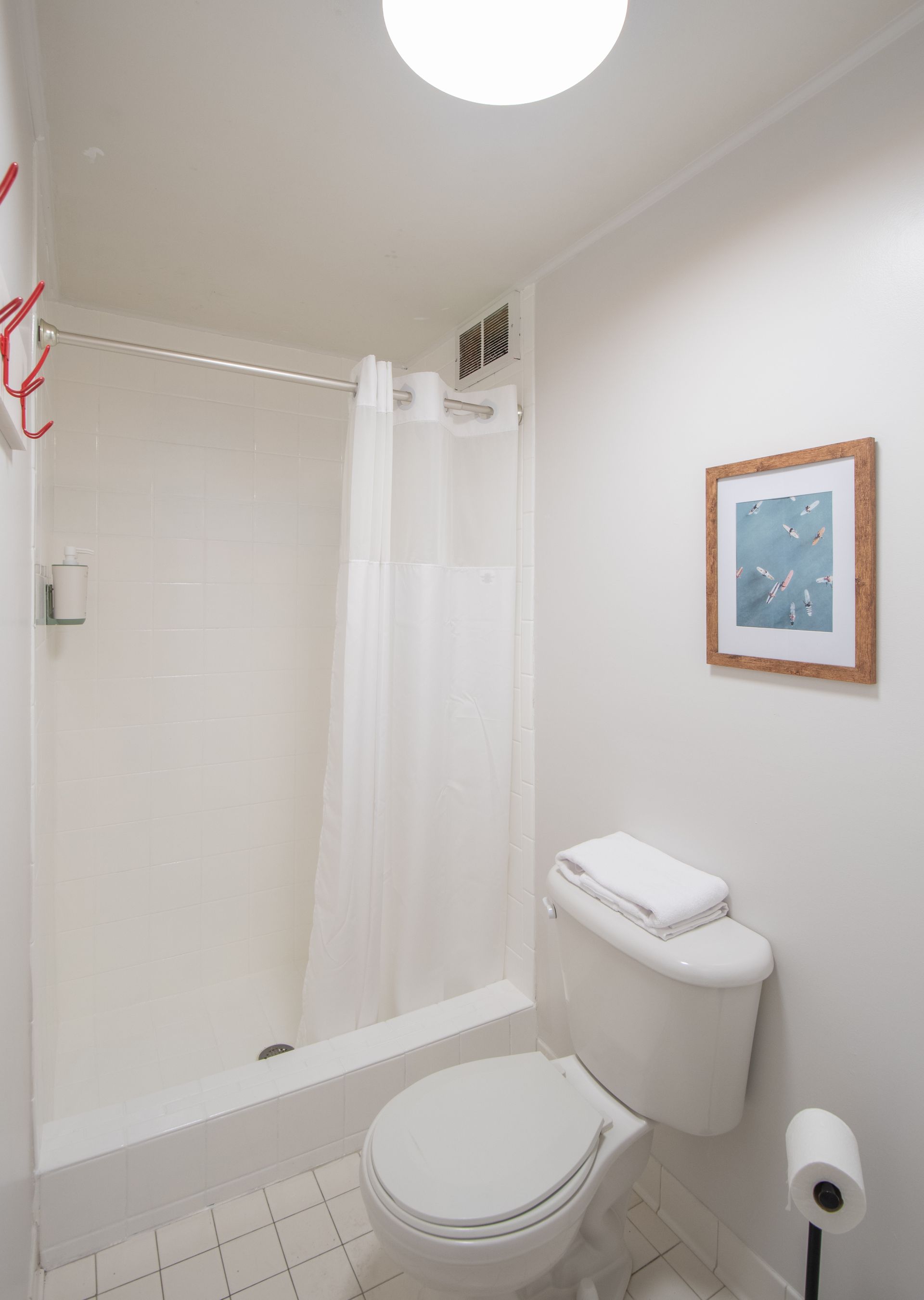 Small bathroom with a toilet, bathtub with shower curtain, wall art, and a toilet paper holder.