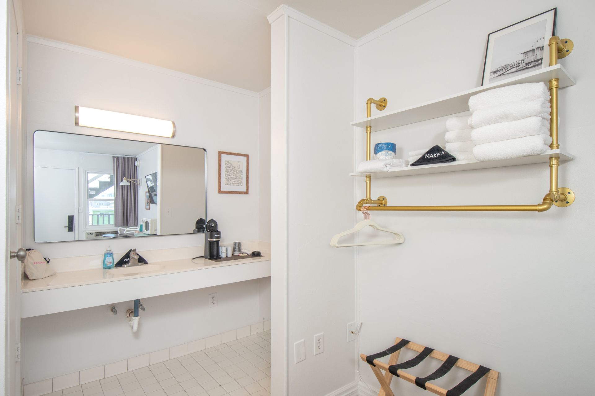 Bright white bathroom with mirror, sink, gold shelving, and striped stool.