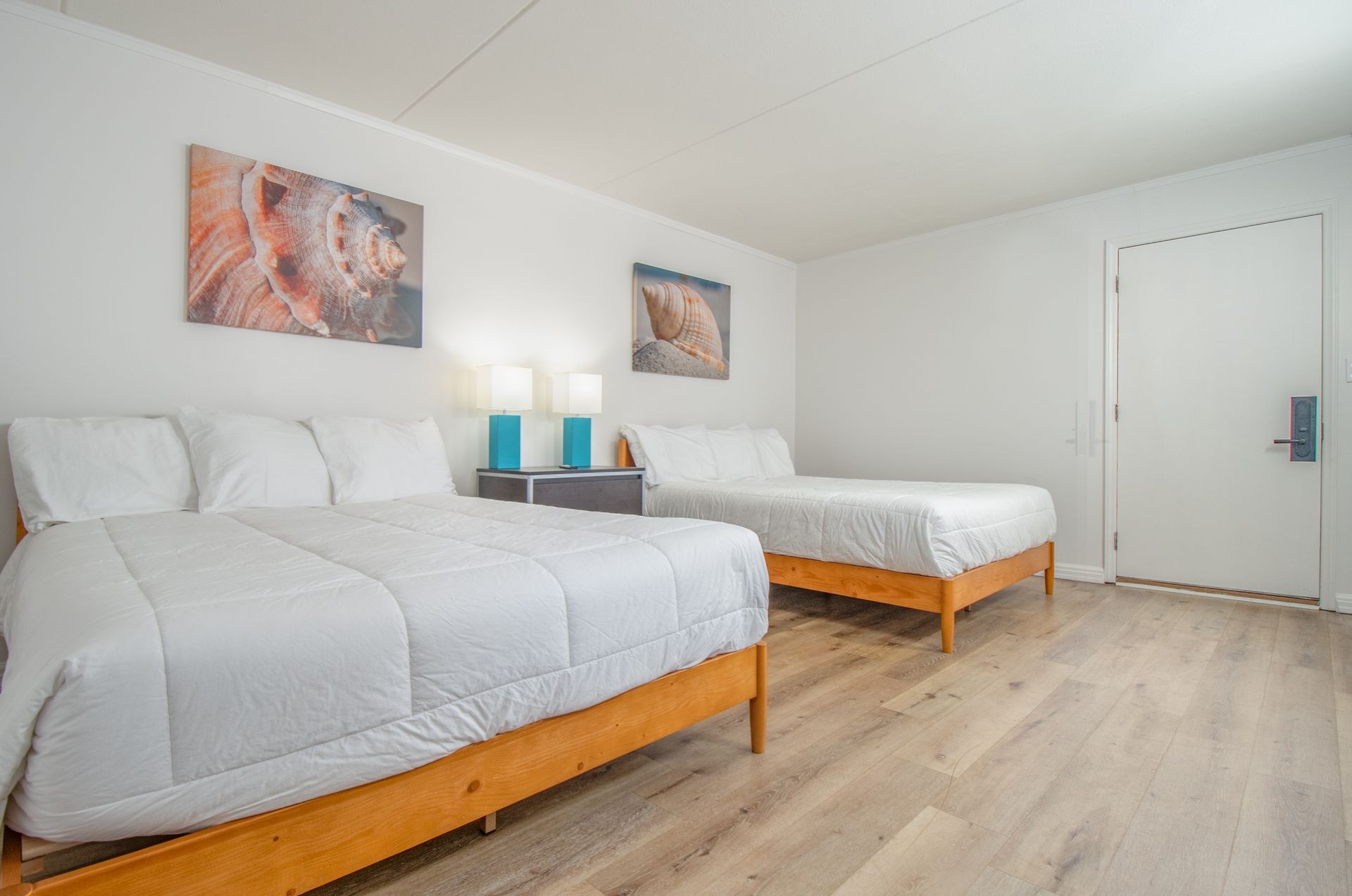 Bright bedroom with two white beds, wood floor, and two abstract wall art pieces