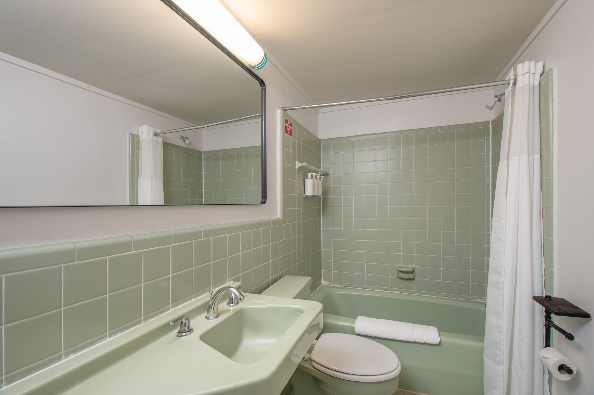 Green-tiled bathroom with bathtub, toilet, sink, mirror, and shower curtain.
