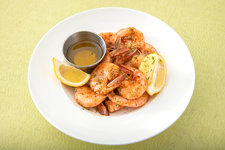 Plated grilled shrimp with lemon wedges and dipping sauce on a white dish